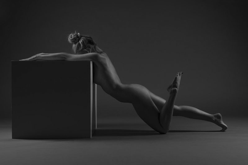 Akrobatisches Aktfoto von Frau die an Würfel lehnt im Fotostudio